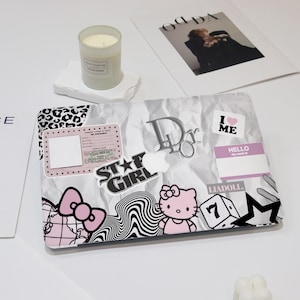 May include: A white laptop with a variety of stickers, including a leopard print, a Hello Kitty sticker, a "Star Girl" sticker, a "Dior" sticker, and a "I Love Me" sticker. The laptop is on a white surface.
