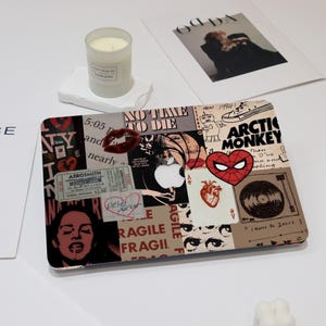 May include: A laptop skin with a collage of images and text. The images include a red heart, a record, a red lips, a Spiderman logo, and a woman's face. The text includes "No Time To Die", "Arctic Monkey", "Peter Parker", and "Fragile".