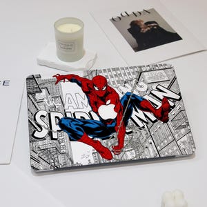 Puede incluir: Una piel para portátil con un diseño de estilo cómic en blanco y negro con Spiderman en un traje rojo y azul balanceándose por una ciudad. El texto "I AM SPIDERMAN" es visible en el diseño.