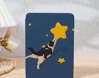 Pode incluir: Uma capa de tablet azul marinho com uma ilustração lúdica de um gato preto e branco alcançando uma grande estrela amarela. Várias estrelas amarelas menores estão espalhadas pela capa.