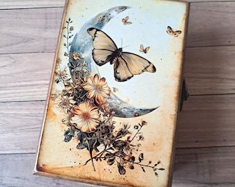 May include: A wooden box with a vintage-inspired design featuring a crescent moon with a butterfly perched on it. The box is decorated with a floral motif in shades of brown and yellow.