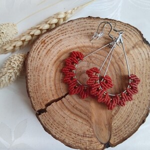 May include: A pair of red beaded earrings with silver hoops and hooks. The earrings are handmade and feature a unique design.