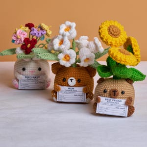 Puede incluir: Tres macetas de flores de ganchillo, cada una con la forma de un animal: un conejito, un oso y otro oso. El conejito sostiene un ramo de flores coloridas. Los osos sostienen carteles que dicen "MOM" y "BEST FRIEND".