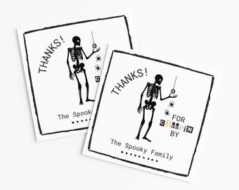 May include: Two square, white Halloween cards with black illustrations and text. Each card shows a skeleton figure holding a string with a spider, the word "THANKS!", and "The Spooky Family".