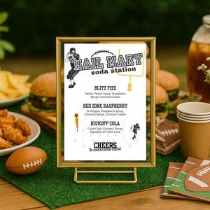 Könnte beinhalten: Ein goldgerahmtes Schild für eine "Hail Mary Soda Station" mit Football-Thema. Das Schild listet Limonadensorten wie "Blitz Fizz" und "Kickoff Cola" auf. Ein Football-förmiges Objekt und eine grüne Oberfläche ergänzen das Thema.