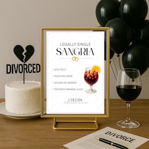 May include: A gold framed sign with "Legally Single Sangria" text and a recipe, a cake with a "Divorced" topper, a glass of red wine, and black balloons. A divorce decree and pen are on the table.