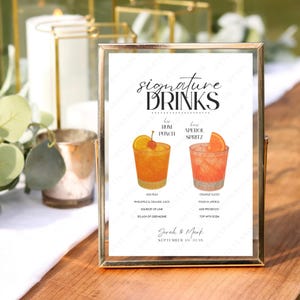 May include: A framed sign with the words "signature DRINKS" in elegant script. The sign features illustrations of two cocktails: Rum Punch and Aperol Spritz, with their ingredients listed below. The sign is personalized with a date and names.