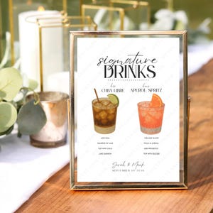 Puede incluir: Un letrero enmarcado en dorado muestra una ilustración en acuarela de dos cócteles: un Cuba Libre y un Aperol Spritz. El letrero dice "signature DRINKS" e incluye los nombres de las bebidas y sus ingredientes. La fecha "September 19 2026" también está impresa.
