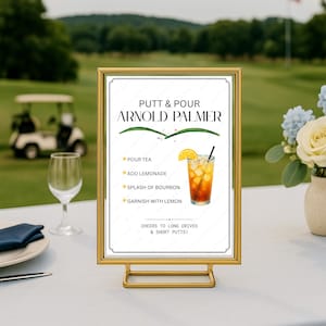 Könnte beinhalten: Ein goldgerahmtes Schild mit dem Text Putt & Pour Arnold Palmer, einem Rezept für ein Getränk mit Tee, Limonade, Bourbon und Zitrone sowie dem Satz Cheers to long drives & short putts, auf einer weißen Oberfläche.