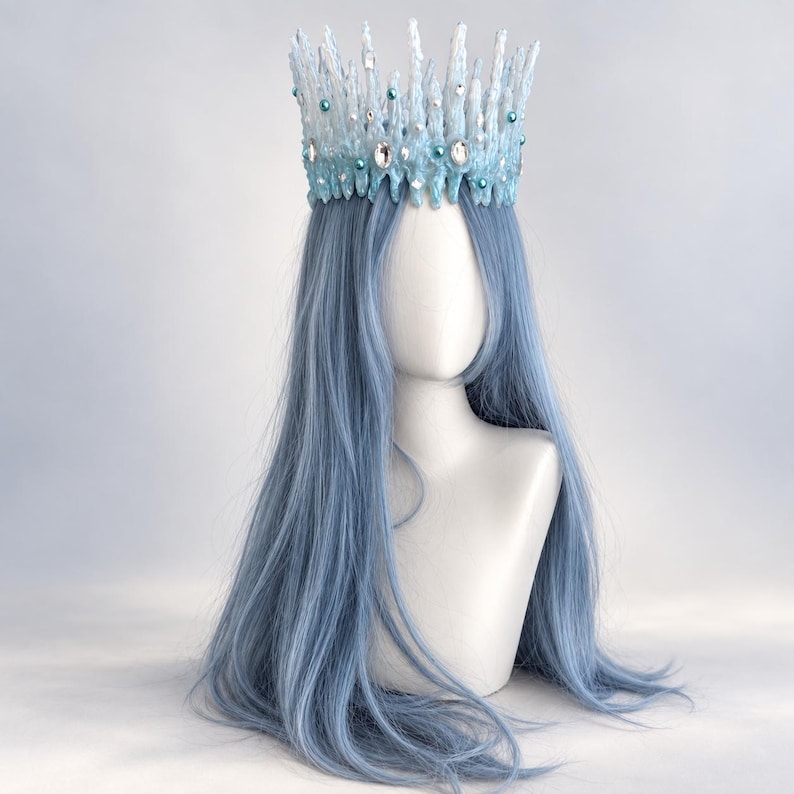 May include: A crown featuring a jagged, ice-like structure in shades of white and light blue, adorned with clear faceted crystals and small round blue beads. The crown is positioned atop a mannequin head with long, straight, light blue hair.