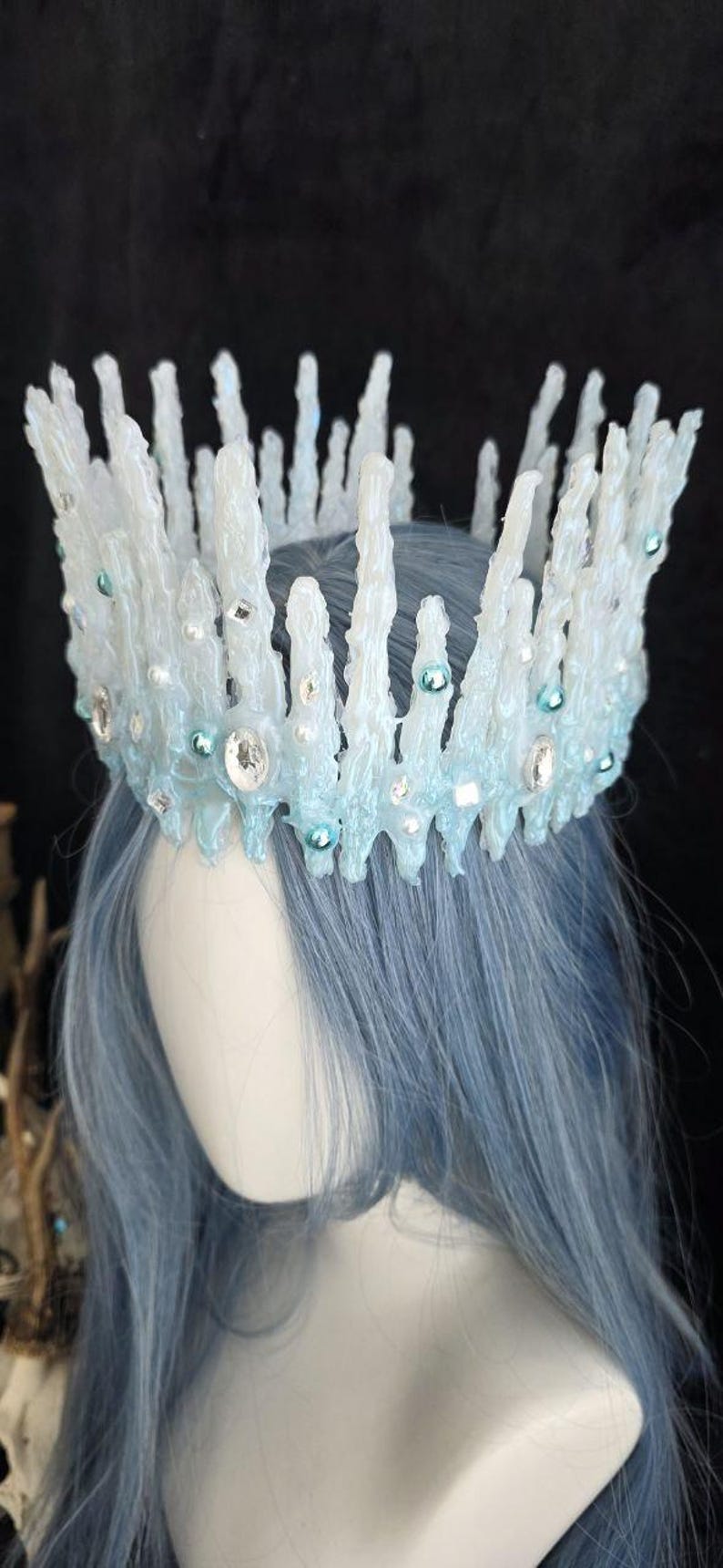 May include: A crown featuring tall, jagged, translucent white and pale blue spikes resembling icicles. The structure is adorned with small, round, light blue beads and clear, faceted crystals embedded throughout the textured, icy surface.