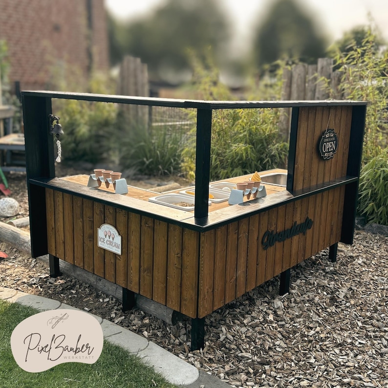 May include: A wooden ice cream stand with a black frame and an "Open" sign. The stand features a counter with containers and ice cream cones. The front of the stand has an "Ice Cream" sign and the word "Waffle" in a cursive font.