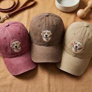 May include: Three baseball caps in maroon, brown, and beige, each featuring an embroidered golden retriever dog face on the front panel. The caps have a structured crown, a curved brim, and a washed fabric texture, showcasing a canine theme.