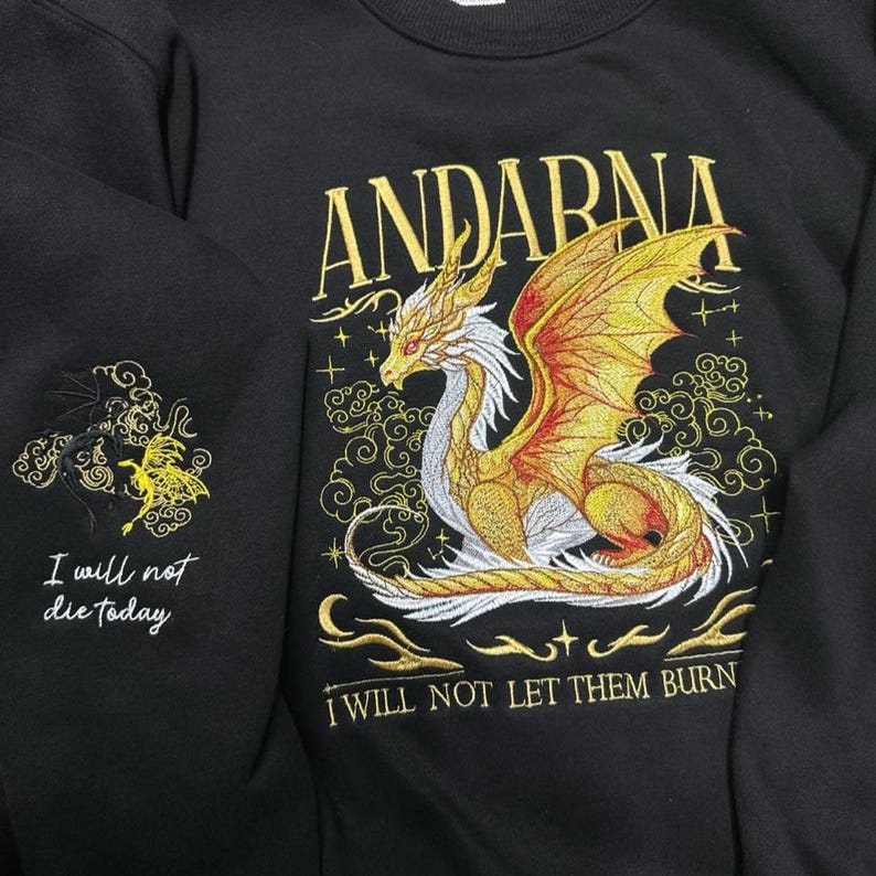 Puede incluir: Sudadera negra con dise&ntilde;o de drag&oacute;n bordado en oro. El drag&oacute;n tiene alas doradas y detalles blancos. El texto "ANDARNA" est&aacute; encima del drag&oacute;n. La manga tiene un dise&ntilde;o de drag&oacute;n m&aacute;s peque&ntilde;o con el texto "I will not die today".