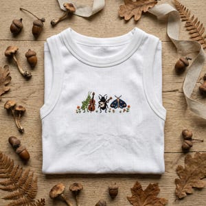 May include: A white ribbed tank top featuring a central embroidered design of three insects playing musical instruments, including a green grasshopper with a cello, a black beetle with a banjo, and a dark blue moth, surrounded by small flowers.