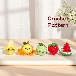 Könnte beinhalten: Eine Sammlung von fünf gehäkelten Obst-Schlüsselanhängern: eine Banane, eine Orange, eine Limette, eine Erdbeere und eine Wassermelone. Jede Frucht hat ein lächelndes Gesicht und ist aus farbigem Garn gefertigt. Der Text "Crochet Pattern" ist im Hintergrund sichtbar.