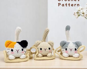 May include: Three crocheted cat plushies sitting on a beige crocheted hammock. The cats are white with different colored markings: orange and black, beige, and gray. The plushies have black eyes and pink cheeks. The text "Crochet Pattern" is written in brown text above the plushies.