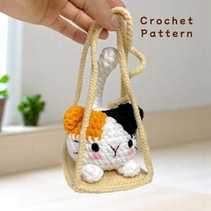 Puede incluir: Un gato de crochet en un columpio, con pelaje naranja, blanco y negro. El gato está sentado en un columpio de crochet con una cuerda de color crema. El texto "Crochet Pattern" es visible en la esquina superior derecha de la imagen.
