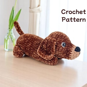 May include: Crochet pattern for a brown dachshund amigurumi toy. The toy is lying on a wooden surface.