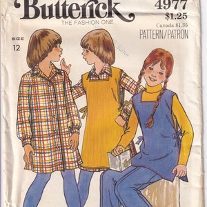 May include: A vintage sewing pattern for children's clothing. The pattern is for a plaid shirt, a yellow pinafore dress, and a blue pinafore dress. The pattern number is 4977 and the price is $1.25. The pattern is from Butterick, The Fashion One.