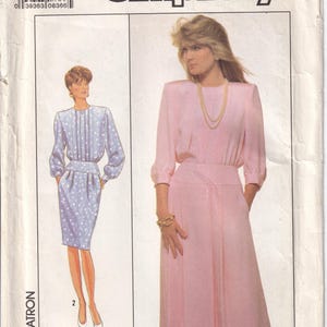 May include: Simplicity sewing pattern featuring two dress designs. One dress is light blue with a white floral pattern, the other is a solid pink dress. The pattern includes sizes 6 and 8. The brand name "Simplicity" is displayed prominently.
