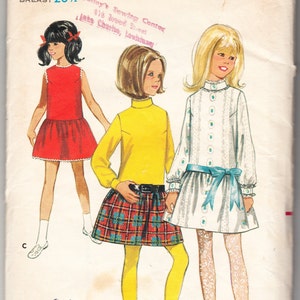 May include: A vintage sewing pattern for girls' dresses. The pattern is for sizes 10 and 28 1/2 inches bust. The pattern includes three different dress styles: a red sleeveless dress, a yellow turtleneck dress with a plaid skirt, and a white dress with a blue sash. The pattern is from Butterick and is number 5053.