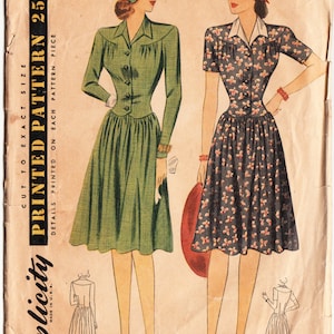 Può includere: Modello di cucito vintage Simplicity per un abito, taglia 12, circonferenza del seno 30. Il modello mostra due donne che indossano l'abito, una in verde tinta unita e l'altra con stampa floreale. Il modello è stampato su carta marrone chiaro con testo nero.