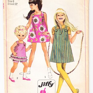 Puede incluir: Un patrón de costura Simplicity vintage para vestidos de niñas. El patrón incluye dos vestidos, uno con estampado floral y el otro con rayas. El patrón está etiquetado como "7709" y "60c".