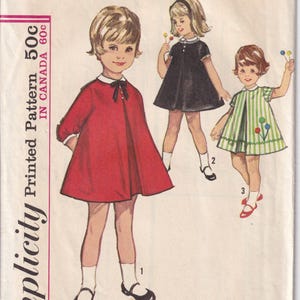 Peut inclure: Patron Simplicity vintage pour robes de taille 3 pour tout-petits. L'illustration montre trois enfants portant différentes robes : une robe rouge avec un col blanc, une robe noire avec un col blanc et une robe à rayures vertes et blanches.