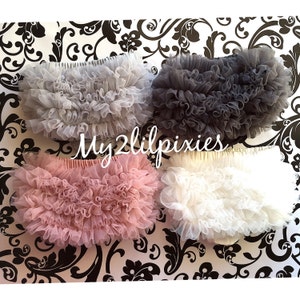 May include: Four pairs of tulle baby bloomers in different colors: gray, black, pink, and white. The bloomers are made of soft, delicate tulle and have multiple layers of ruffles.