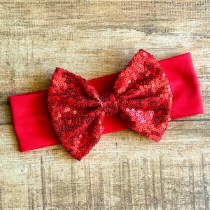 May include: Red sequin bow headband. The headband is made of a soft, stretchy fabric and features a large, sparkly bow.