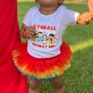 Puede incluir: Una ni&ntilde;a peque&ntilde;a con una camiseta blanca con el texto "Kyndall Birthday Girl" y una imagen de dibujos animados de personajes del programa "Cocomelon". La ni&ntilde;a tambi&eacute;n lleva una falda de tul roja y arco&iacute;ris.