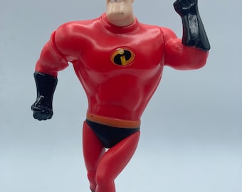 May include: Red and black plastic action figure of Mr. Incredible from the Disney Pixar movie The Incredibles. The figure is posed with one arm raised and a fist clenched. The figure has a black mask and a black belt with a yellow symbol.