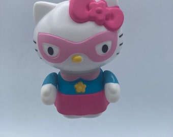 May include: A white Hello Kitty keychain with a pink bow, pink mask, and blue and pink superhero costume.