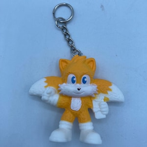 May include: A Tails the Fox keychain figurine. The figure is orange with white accents on the wings, chest, and shoes. It has blue eyes and a silver chain and keyring.