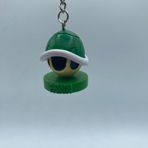 May include: Green and white shell-shaped keychain with a yellow face and the word "PAWN" printed on the base.