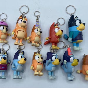 May include: A collection of colorful cartoon dog keychains. Each keychain features a different character design with various outfits and accessories. The keychains are made of plastic and have silver metal key rings attached.