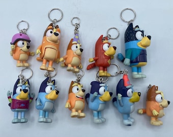 May include: A collection of colorful cartoon dog keychains. Each keychain features a different character design with various outfits and accessories. The keychains are made of plastic and have silver metal key rings attached.