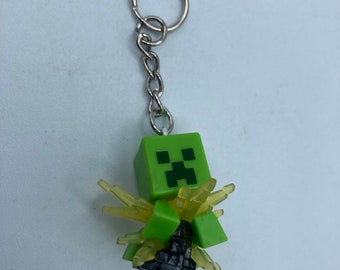 May include: A green Minecraft Creeper keychain with a yellow glow effect. The keychain is attached to a silver metal chain and ring.