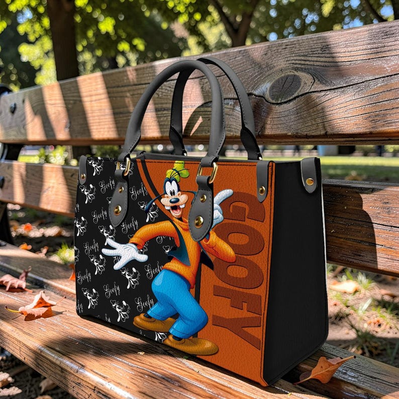 May include: A black, brown, and orange tote bag featuring a cartoon image of Goofy. The bag has black handles and a black side panel. The word "Goofy" is printed in large orange letters on the side of the bag.