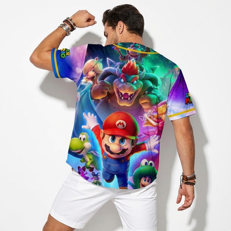 May include: A short-sleeved, colorful shirt featuring a vibrant graphic of Mario and other characters from the Super Mario video game series. The shirt has blue sleeves with yellow stripes and the words "Super Mario" printed on the sleeve.