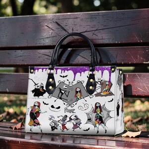May include: White tote bag featuring a Halloween-themed design with characters and imagery from the movie. The bag has black handles and purple accents. The design includes Jack Skellington, Sally, and other characters.