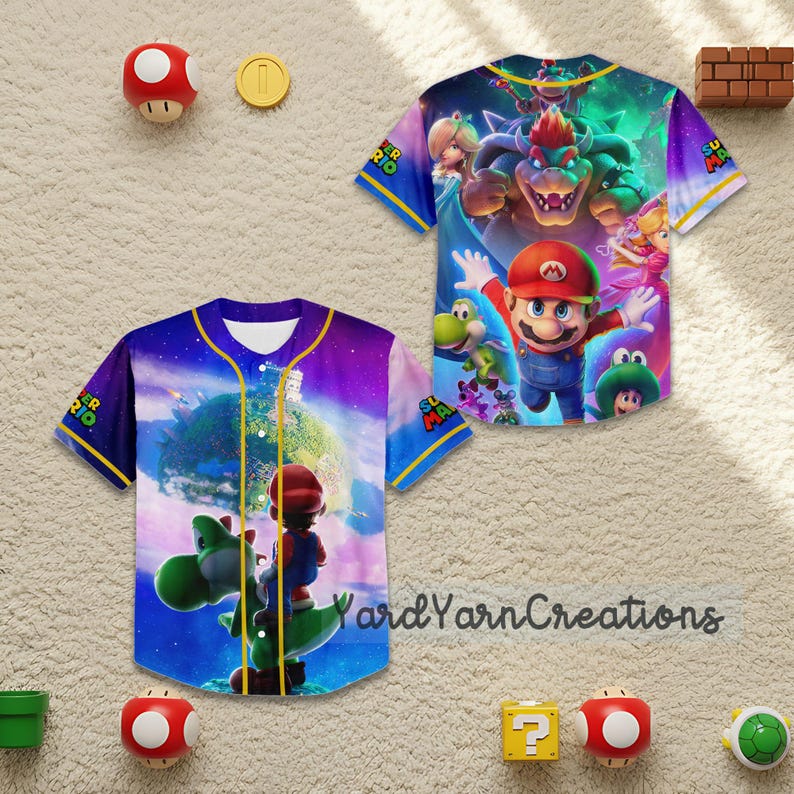 May include: Two short-sleeved baseball jerseys with colorful graphics of characters from the Super Mario Bros. movie. The jerseys have blue and yellow accents, and the text "Super Mario" is visible on the sleeves. The background includes various Super Mario-themed decorations.