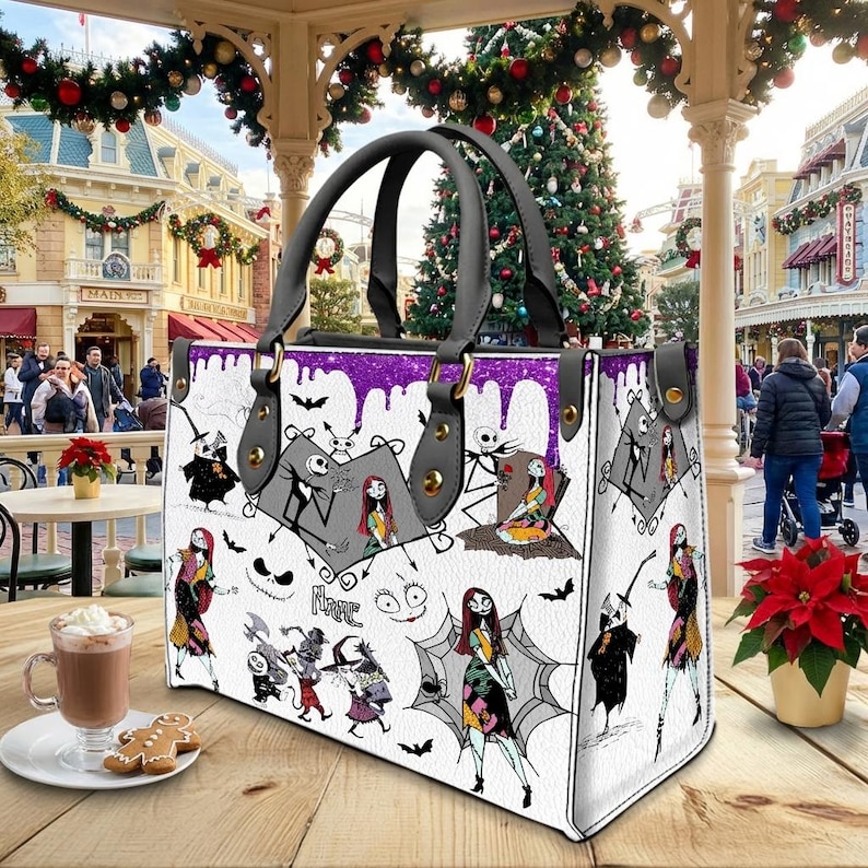 May include: White tote bag featuring illustrations of characters from "The Nightmare Before Christmas." The bag has black handles and a purple glitter trim. The bag is sitting on a wooden table with a cup of hot chocolate and a gingerbread cookie.