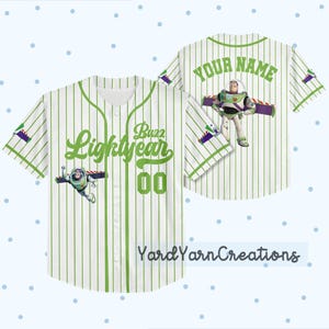 K&ouml;nnte beinhalten: Wei&szlig;-gr&uuml;nes Baseball-Trikot mit Nadelstreifen und Buzz Lightyear aus Toy Story. Das Trikot hat gr&uuml;ne Akzente, die Worte "Buzz Lightyear" und die Nummer "00" auf der Vorderseite. Auf der R&uuml;ckseite des Trikots stehen die Worte "Your Name" und eine Buzz Lightyear-Grafik.