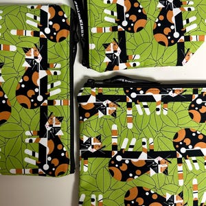 Puede incluir: Tres estuches con cremallera con un patr&oacute;n repetido de gatos estilizados en negro, naranja y blanco sobre un fondo de hojas verdes. Los estuches var&iacute;an en tama&ntilde;o y est&aacute;n dispuestos sobre una superficie blanca. El dise&ntilde;o incluye el texto "stolenMinute".