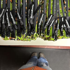 Puede incluir: Primer plano de varias bolsas con cremallera y cremalleras y tiradores negros. Las bolsas tienen una tela estampada verde y negra. Cada tirador de cremallera tiene el texto "StolenMinutes" impreso.