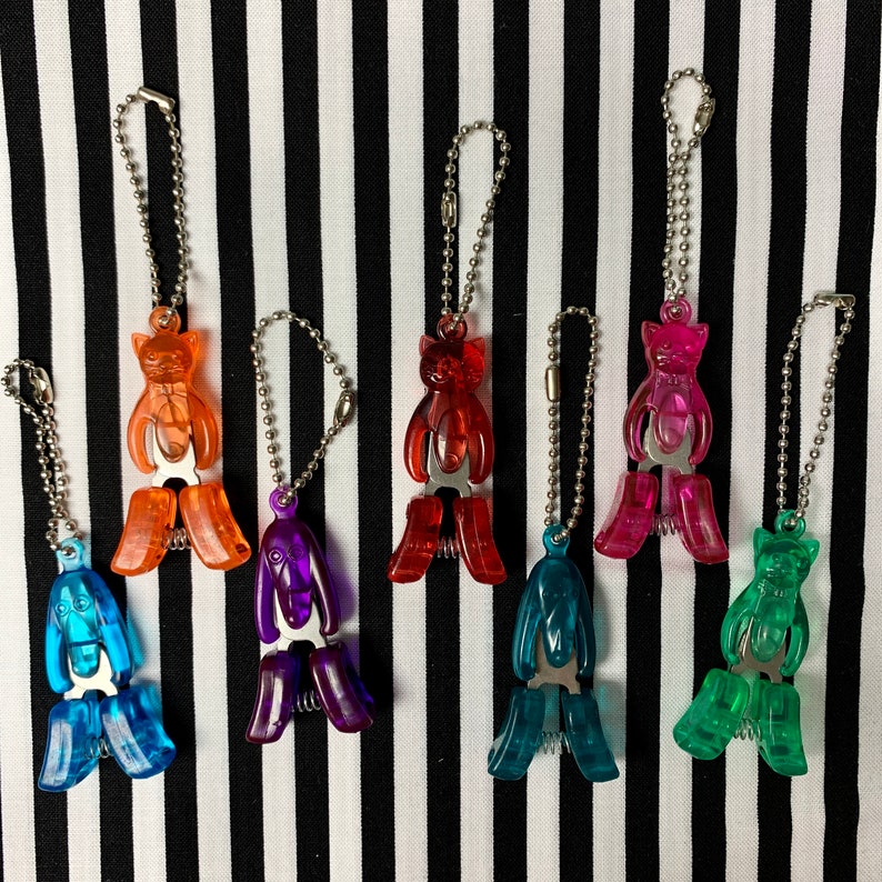 K&ouml;nnte beinhalten: Sieben bunte katzenf&ouml;rmige Schl&uuml;sselanh&auml;nger mit silbernen Ketten. Die Schl&uuml;sselanh&auml;nger sind aus Kunststoff und haben einen federbelasteten Clip. Die Katzen sind in verschiedenen Farben, darunter Orange, Rot, Lila, Rosa, Blau und Gr&uuml;n.