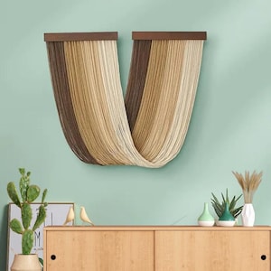 May include: A wall hanging made of brown and beige yarn, with a U-shaped design. The hanging is attached to a wooden frame.