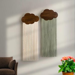 May include: Two wooden cloud-shaped wall hangings with strings of yarn hanging down. The cloud on the left has white yarn and the cloud on the right has green yarn.